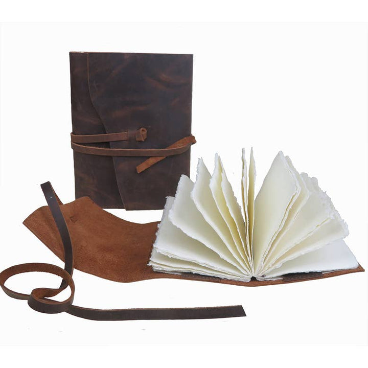 Nahkakantinen muistikirja avoimena ja suljettuna; kuvassa läppä ja pitkä nahkanauha. / Leather notebook shown open and closed, with a flap and long leather tie.