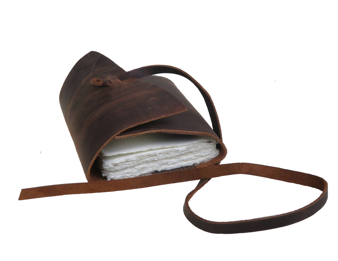 Nahkamuistikirjan sivukuva, jossa näkyvät käsintehdyn paperin epätasaiset reunat ja nahkanauha. / Side view of a leather notebook showing the uneven edges of the handmade paper and a leather tie.