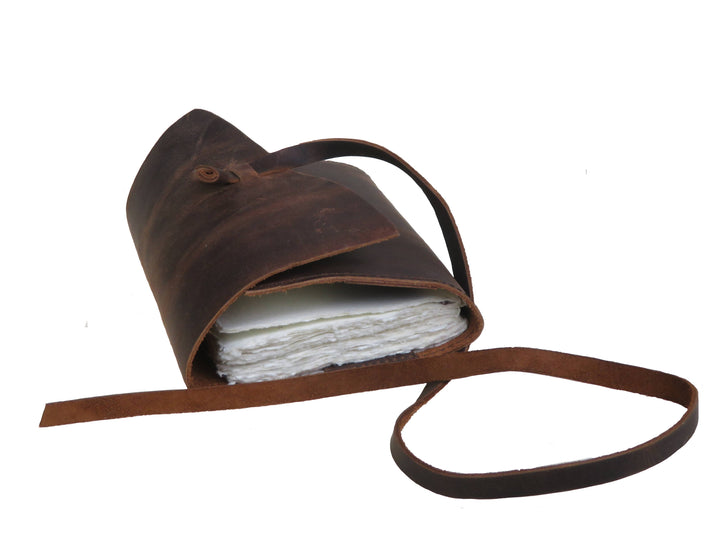 Nahkamuistikirjan sivukuva, jossa näkyvät käsintehdyn paperin epätasaiset reunat ja nahkanauha. / Side view of a leather notebook showing the uneven edges of the handmade paper and a leather tie.