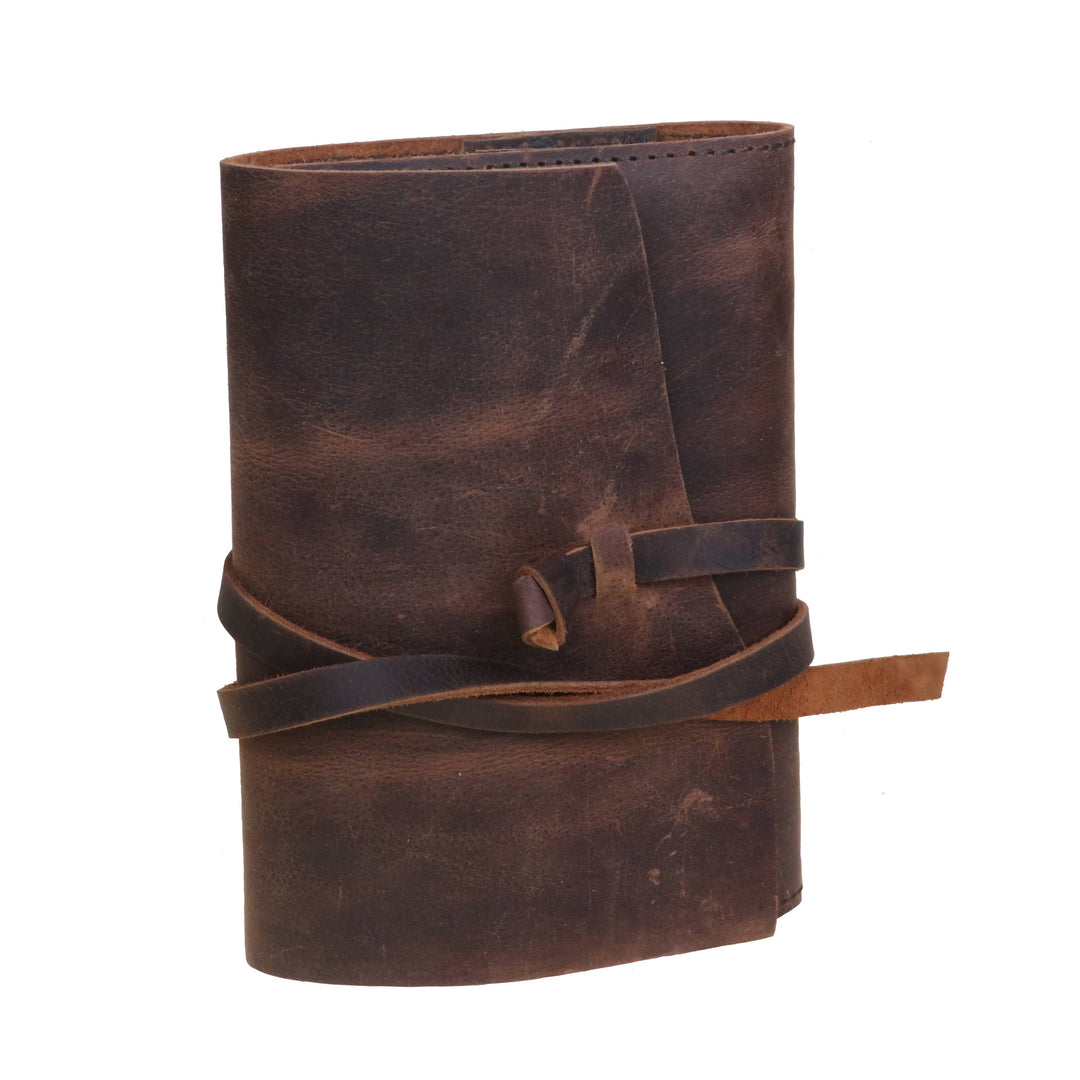 Ruskea nahkamuistikirja suljettuna, kannen yli kulkeva läppä ja nahkanauha. / Closed brown leather notebook with a cover flap and leather tie.