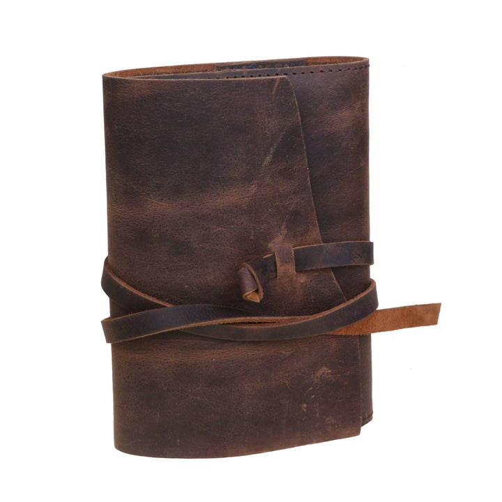 Ruskea nahkamuistikirja suljettuna, kannen yli kulkeva läppä ja nahkanauha. / Closed brown leather notebook with a cover flap and leather tie.