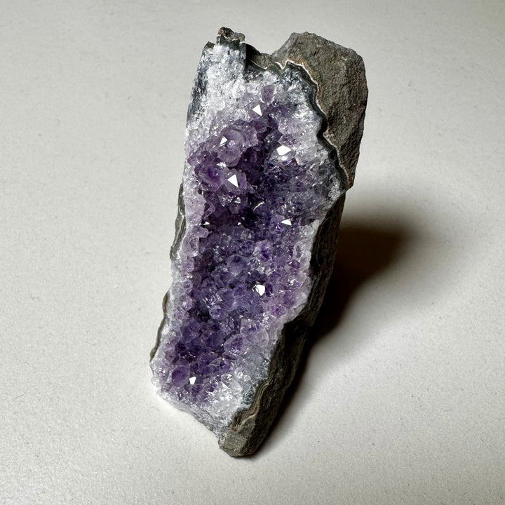 Ametistiklusteri oikealta kuvattuna; kiteiden syvyys ja peruskiven vihreänharmaat sävyt korostuvat. -  Amethyst cluster photographed from the right; the depth of the crystals and the greenish-grey tones of the base rock are emphasized.