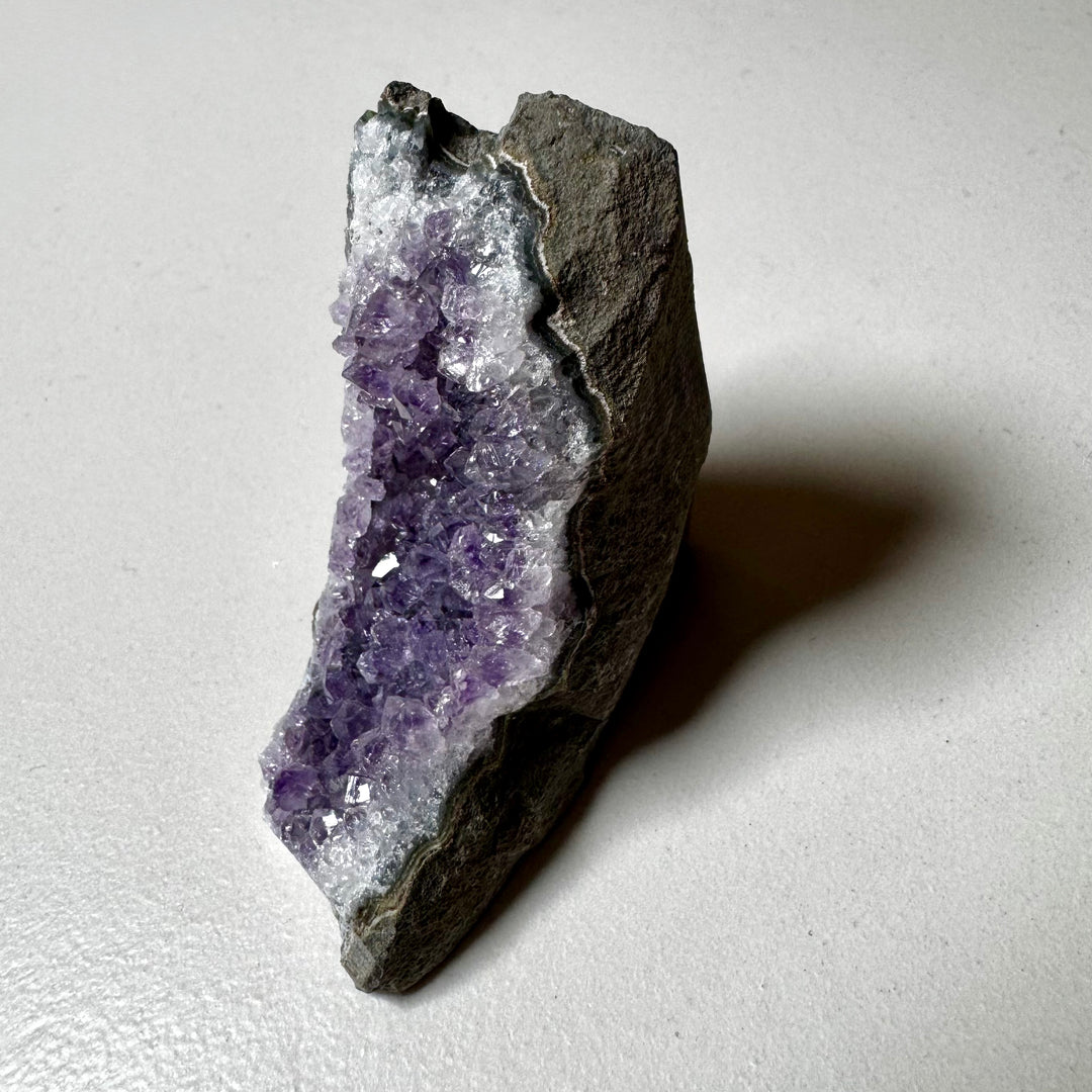 Ametistiklusteri oikealta kuvattuna; kiteiden syvyys ja peruskiven vihreänharmaat sävyt korostuvat. - Amethyst cluster photographed from the right; the depth of the crystals and the greenish-grey tones of the base rock are emphasized.