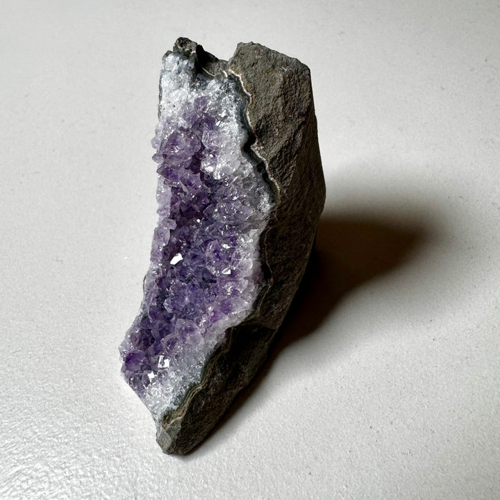 Ametistiklusteri oikealta kuvattuna; kiteiden syvyys ja peruskiven vihreänharmaat sävyt korostuvat. - Amethyst cluster photographed from the right; the depth of the crystals and the greenish-grey tones of the base rock are emphasized.