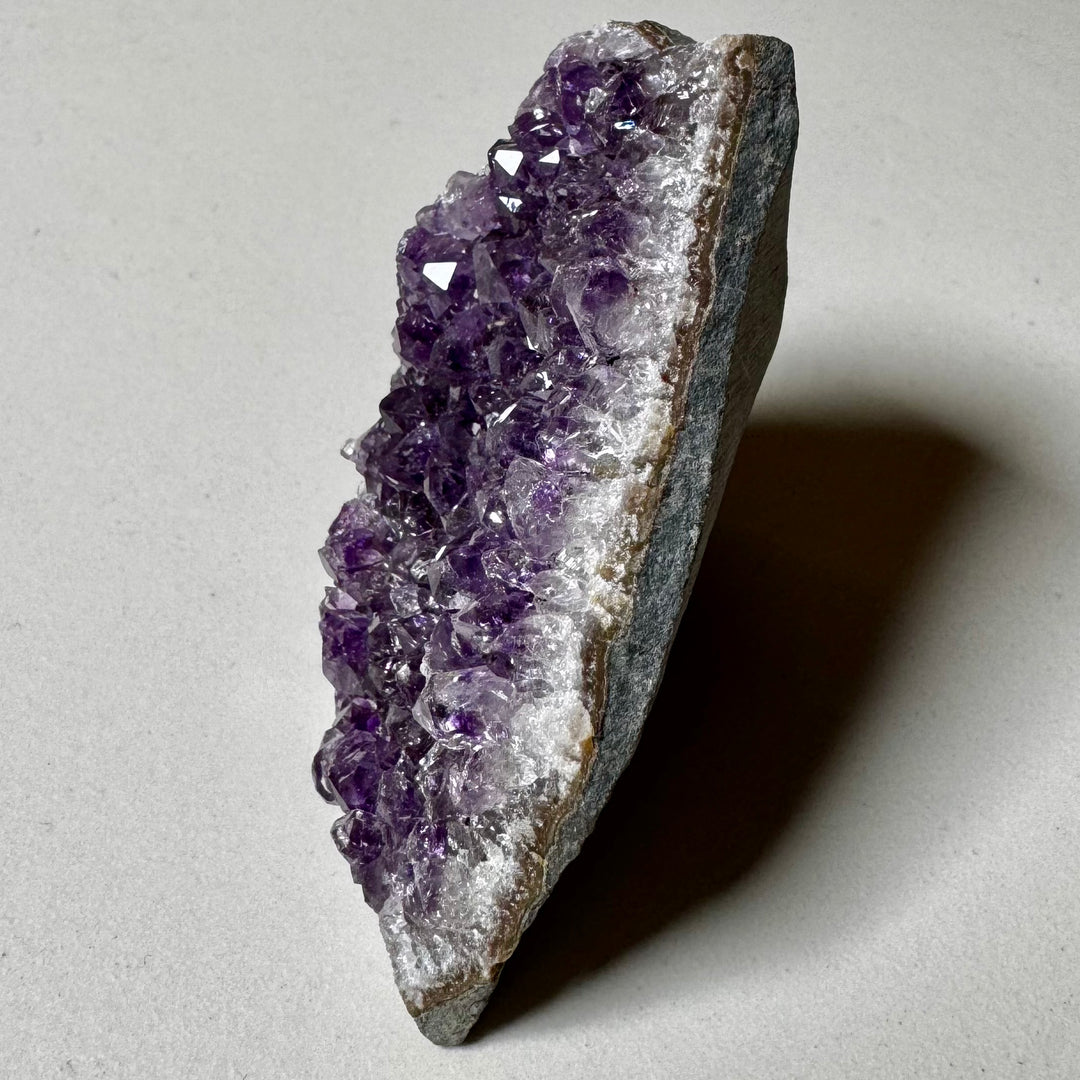 Ametistiklusteri oikealta kuvattuna; kiteiden syvyys ja peruskiven vihreänharmaat sävyt korostuvat. -  Amethyst cluster photographed from the right; the depth of the crystals and the greenish-grey tones of the base rock are emphasized.