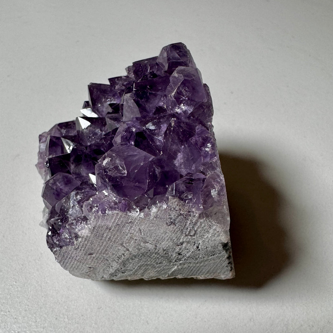 Ametistiklusteri oikealta kuvattuna; kiteiden syvyys ja peruskiven vihreänharmaat sävyt korostuvat. - Amethyst cluster photographed from the right; the depth of the crystals and the greenish-grey tones of the base rock are emphasized.