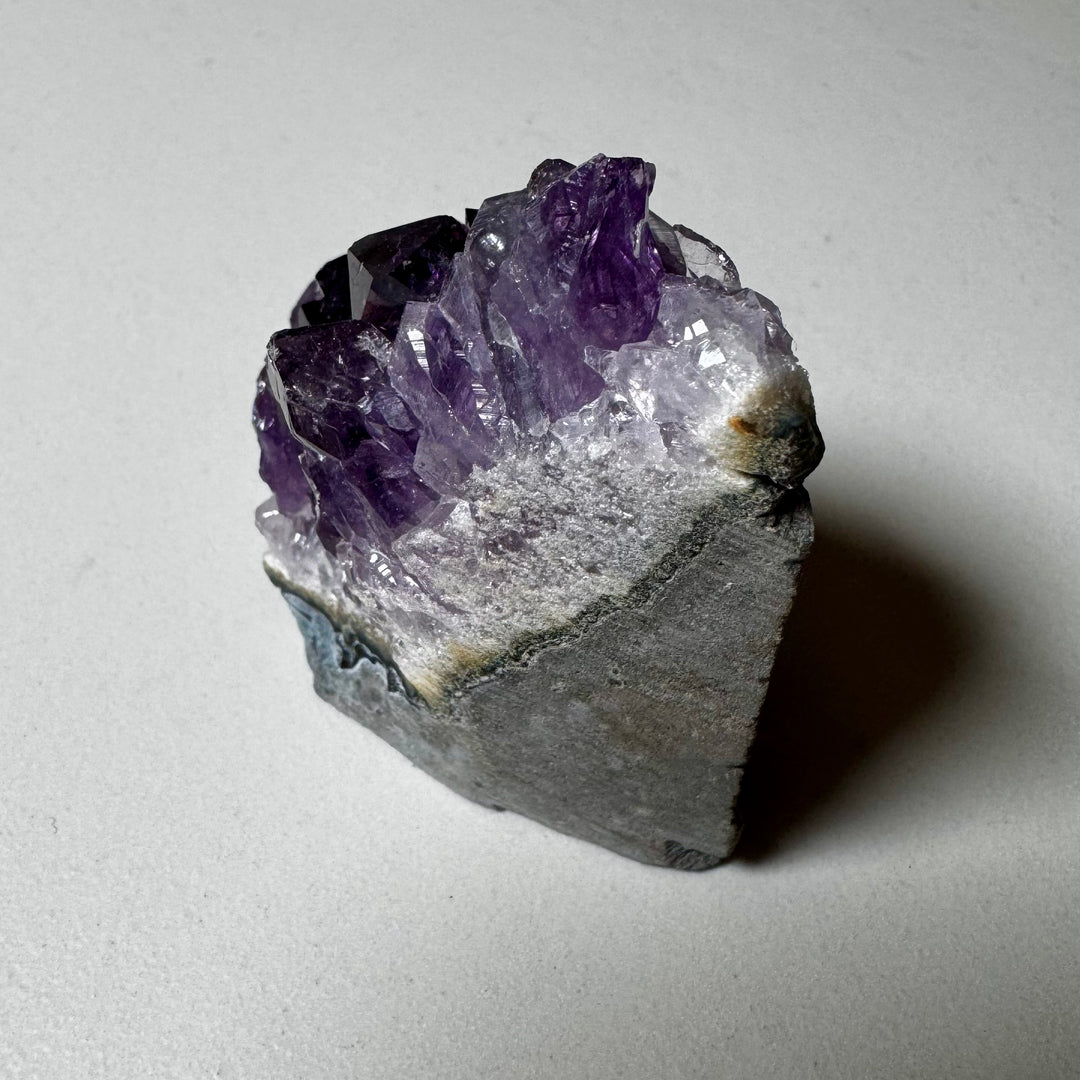 Ametistiklusteri oikealta kuvattuna; kiteiden syvyys ja peruskiven vihreänharmaat sävyt korostuvat. - Amethyst cluster photographed from the right; the depth of the crystals and the greenish-grey tones of the base rock are emphasized.