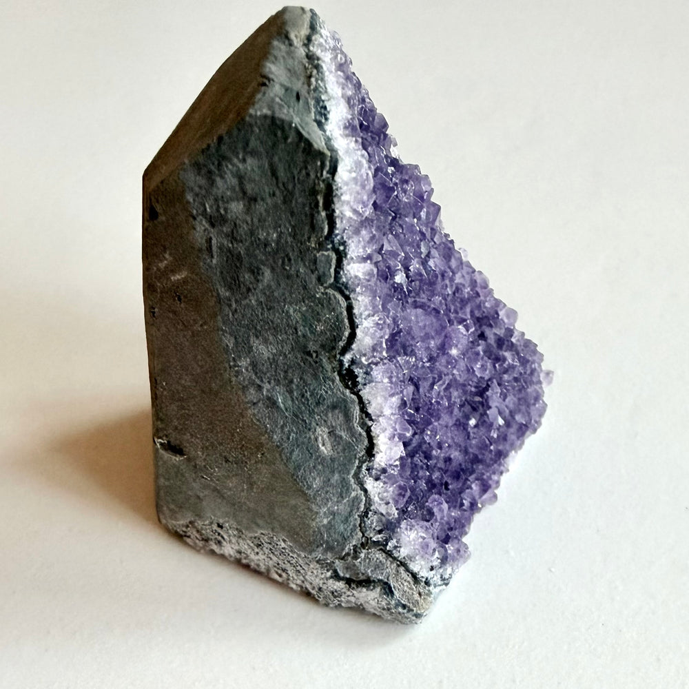 Ametistigeodin palanen kuvattuna sivulta. Näkyvillä geodin rosoinen sisäpinta, kaunis violetti värisävy geodin isäntäkivi.