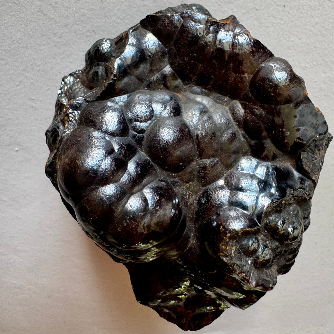 Botryoidinen hematiitti – rypälemäinen raakakivi, jossa tummanharmaa metallinkiilto ja sileä, kumpuileva pinta. -  Botryoidal hematite – raw mineral specimen with dark metallic luster and smooth, rounded surface.