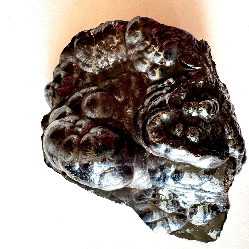 Hematiitin kiiltävä pinta lähikuvassa, pyöreitä toisiinsa sulautuneita kumpuja. -  Close-up of hematite’s glossy surface showing rounded, merged formations.