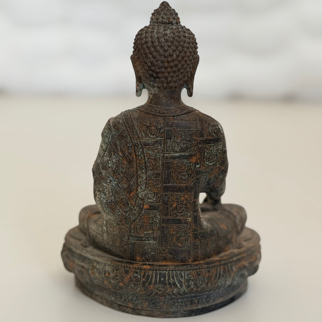 Buddha-patsaan takaosa toisesta kuvakulmasta; hienojakoinen ornamenttikuviointi metallipinnassa. - Rear view of the Buddha statue from a slightly different angle, highlighting the fine ornamental detailing on the metal surface.