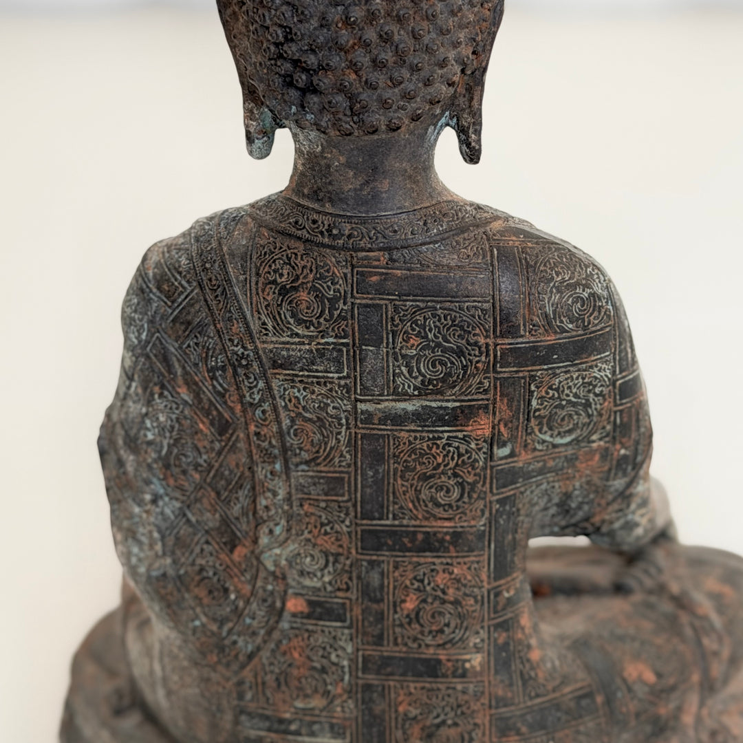 Buddha-patsaan takaosa lähikuvassa; yksityiskohtaisesti koristeltu kaapu ja patinoitu tumma metallipinta. - Close-up of the back of the Buddha statue, showing the intricately decorated robe and dark patinated metal surface.
