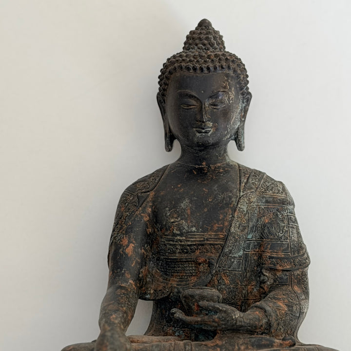 Etukuva Buddha-patsaasta vaaleaa taustaa vasten; tumma patinoitu metallipinta ja rauhallinen ilme. - Frontal view of the Buddha statue against a light background, showing the dark patinated metal surface and calm expression.