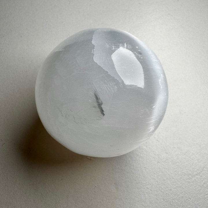 Kirkas ja läpikuultava seleniittipallo, jonka pinta heijastaa valoa silkkimäisesti. - Clear and translucent selenite sphere with a light-reflecting, silky surface.