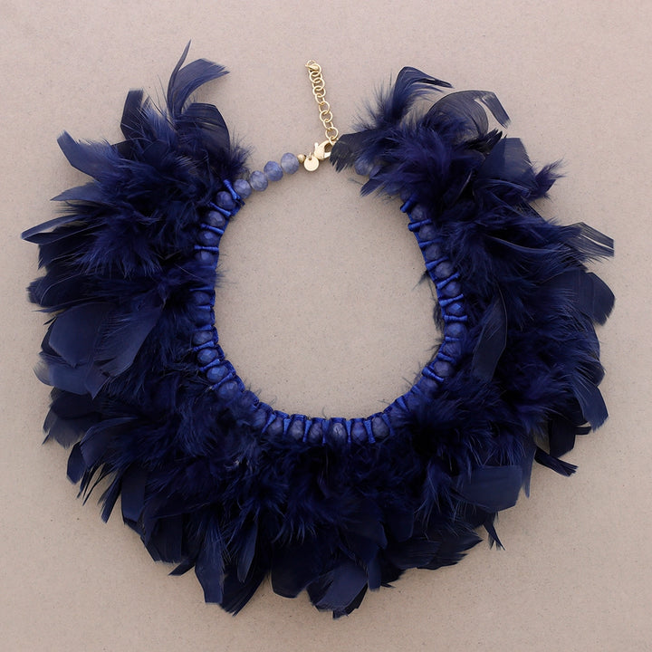 Syvän sininen sulkakaulakoru, jossa luonnonsulat on punottu helmillä koristeltuun nauhapohjaan. - Deep blue feather necklace with natural feathers woven into a beaded ribbon base.