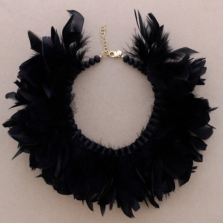 Musta sulkakaulakoru, jossa luonnonsulat on punottu helmillä koristeltuun nauhapohjaan. Korun väri symboloi suojaa ja muutosta. - Black feather necklace with natural feathers woven into a beaded ribbon base. The black color symbolizes protection and transformation.