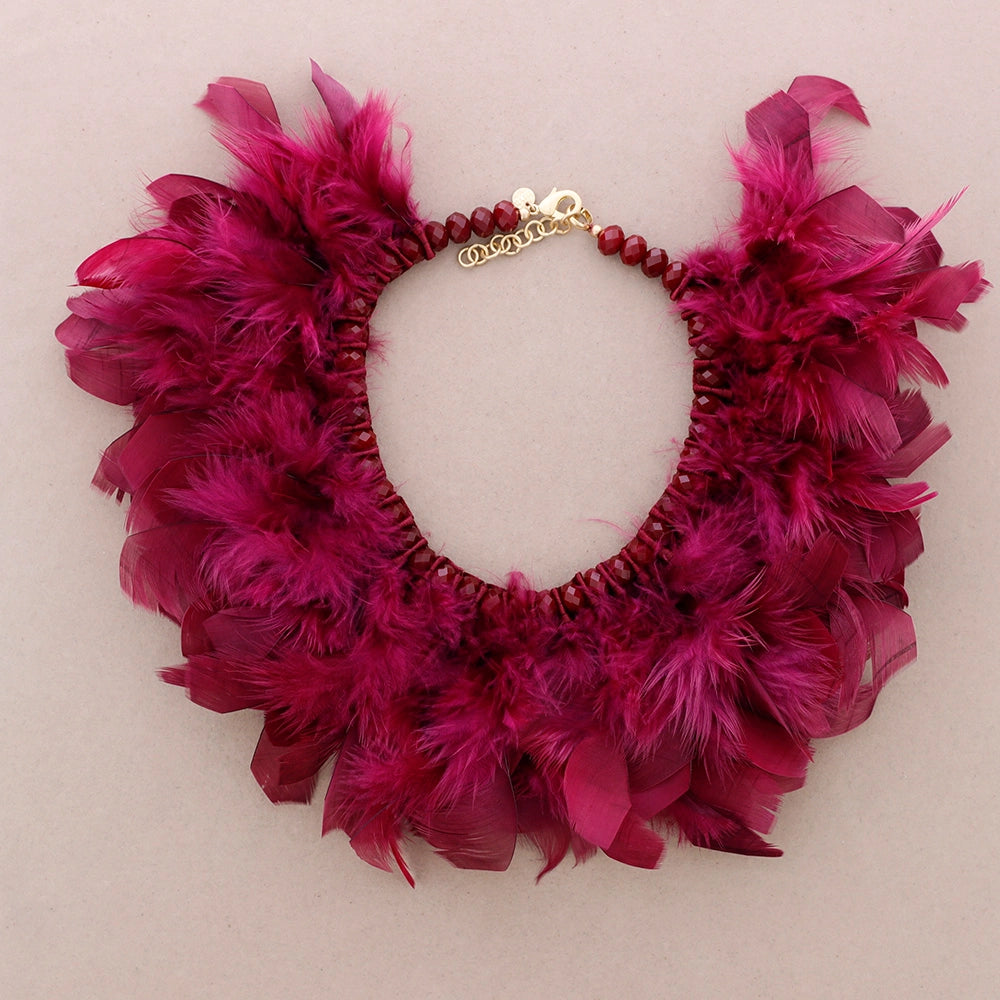 Fuksian punainen sulkakaulakoru, jossa luonnonsulat on punottu helmillä koristeltuun nauhapohjaan. - Fuchsia red feather necklace with natural feathers woven into a beaded ribbon base.