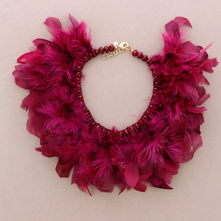 Fuksian punainen sulkakaulakoru, jossa luonnonsulat on punottu helmillä koristeltuun nauhapohjaan. - Fuchsia red feather necklace with natural feathers woven into a beaded ribbon base.