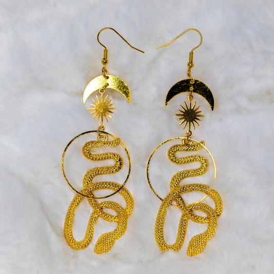 Kullanväriset käärmekorvakorut, joissa näkyy käärme, aurinko ja kuu kokonaisuudessaan. - Golden colored snake earrings featuring a snake, sun, and moon in full view.