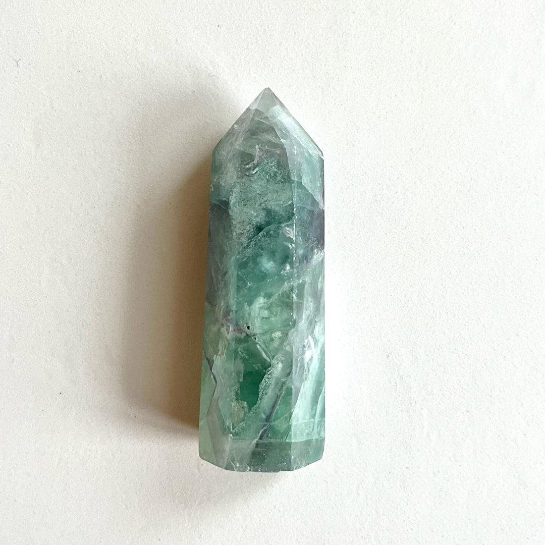 Kuvassa vihreä fluoriittitorni vaaka-asennossa tasolla. - A green fluorite tower placed sideways on a table.