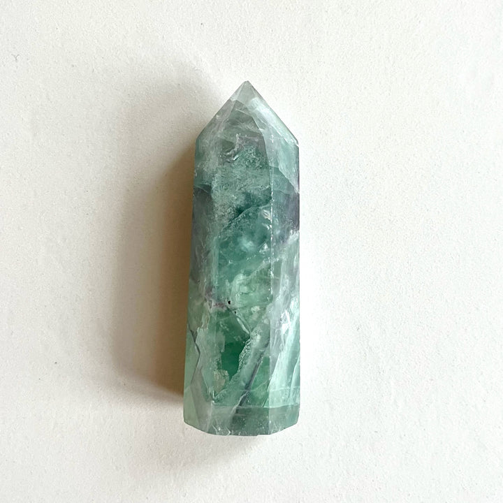 Kuvassa vihreä fluoriittitorni vaaka-asennossa tasolla. - A green fluorite tower placed sideways on a table.