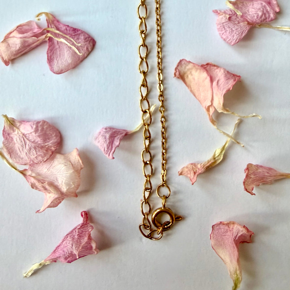 Kultaisen kaulakorun teräsketju ja lukko yksityiskohtaisessa lähikuvassa - Close-up of gold necklace's steel chain and clasp with delicate flower petals