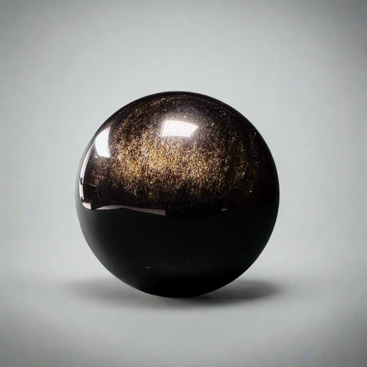 Kullanhohto-obsidiaanipallo, jossa kultainen hohde korostaa laavalasin ainutlaatuista pintaa. - Gold sheen obsidian sphere with a golden sheen highlighting the unique surface of the volcanic glass.