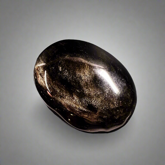  Goldsheen-obsidiaani kämmenkivi, kiiltävä pinta heijastaa kultaisia sävyjä. - Goldsheen obsidian palm stone with a shiny surface reflecting golden hues.