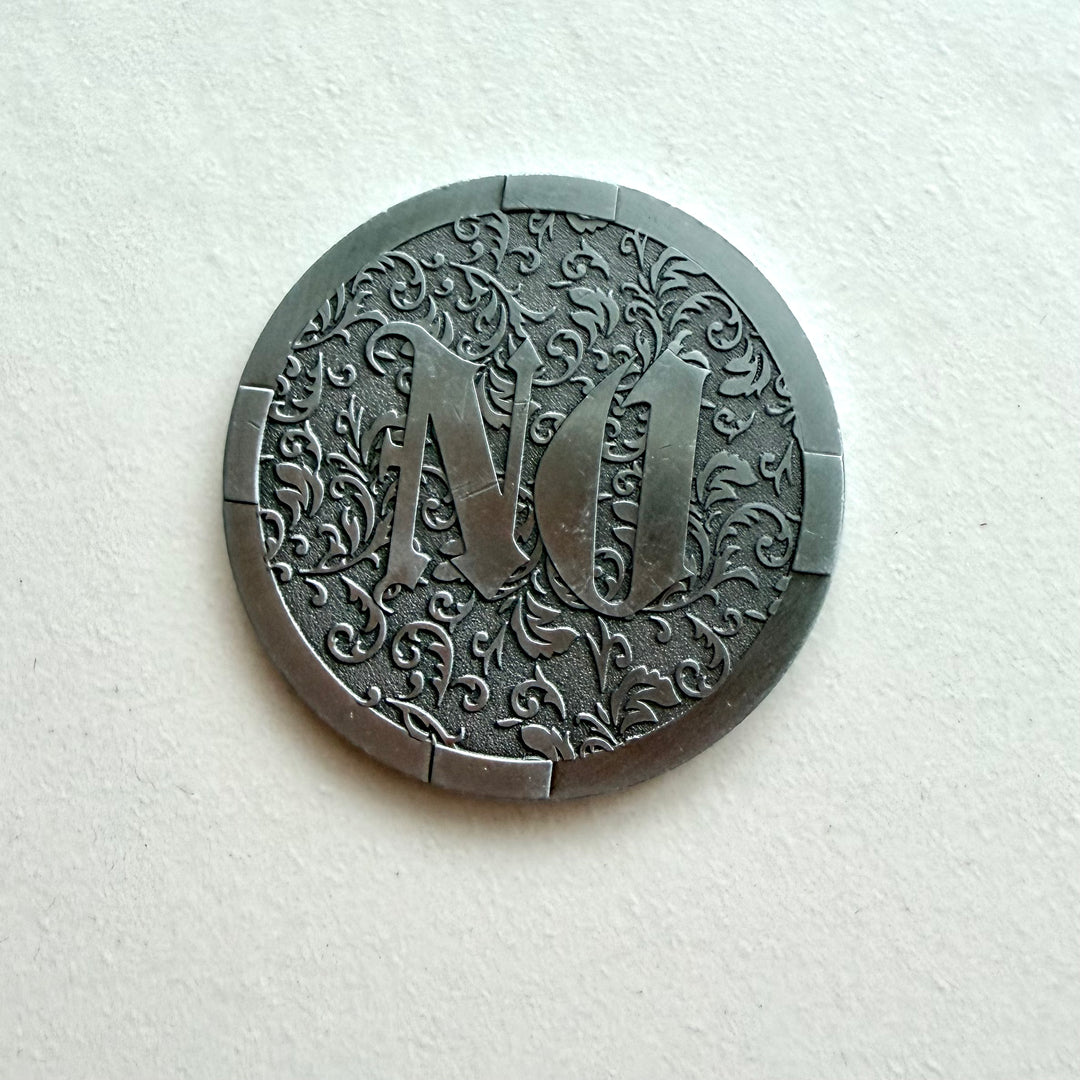 Hopeanvärisen YES / NO -päätöskolikon NO-puoli, jossa on koristeellinen kasviaiheinen kuviointi.
