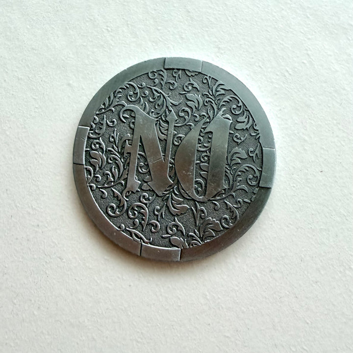 Hopeanvärisen YES / NO -päätöskolikon NO-puoli, jossa on koristeellinen kasviaiheinen kuviointi.