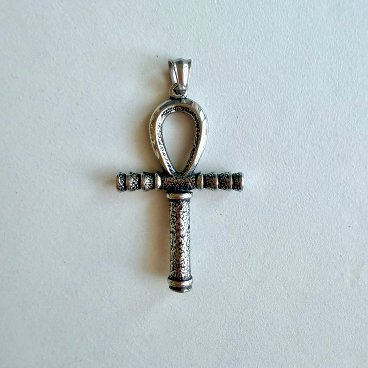 Hopeanvärinen ruostumattomasta teräksestä valmistettu Ankh-amuletti mustatuilla yksityiskohdilla vaalealla taustalla.