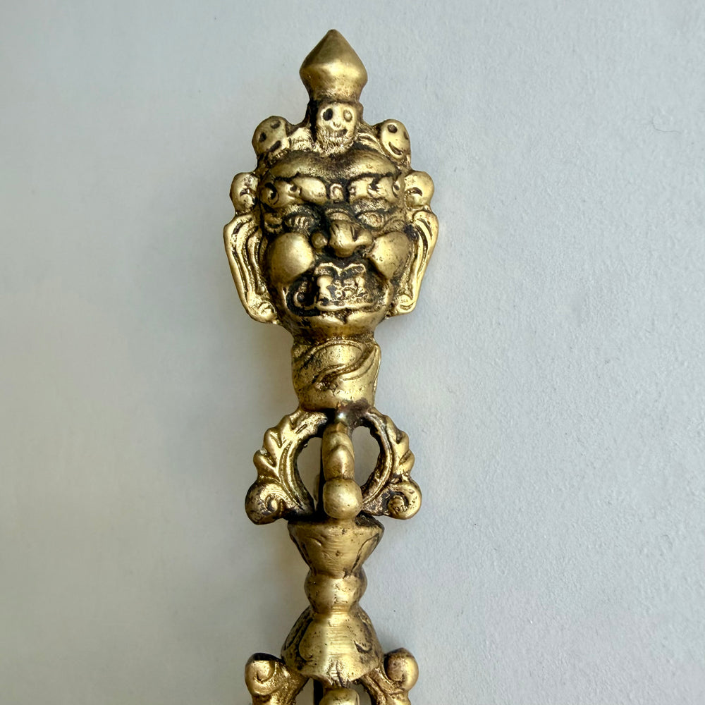 Lähikuva phurban raivokkaista kasvoista, kallokoristeista ja kahvan yläosan vajra-aiheesta. / Close-up of the phurba’s wrathful face, skull ornaments and upper vajra handle.
