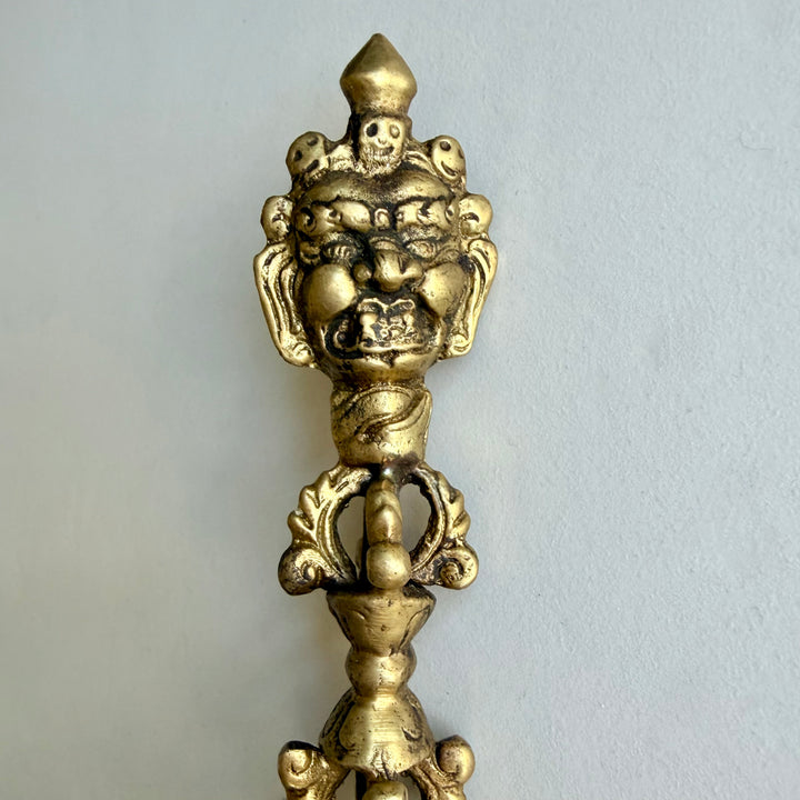 Lähikuva phurban raivokkaista kasvoista, kallokoristeista ja kahvan yläosan vajra-aiheesta. / Close-up of the phurba’s wrathful face, skull ornaments and upper vajra handle.