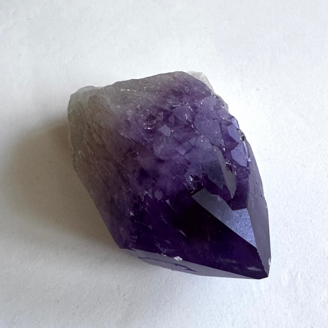 Detailed tip of amethyst cathedral quartz, with deepening color toward the apex symbolizing spiritual growth.
FIN: Ametisti-katedraalikvartsin kärki yksityiskohtaisesti, tummuva sävy kohti huippua, symboloiden henkistä kasvua.
