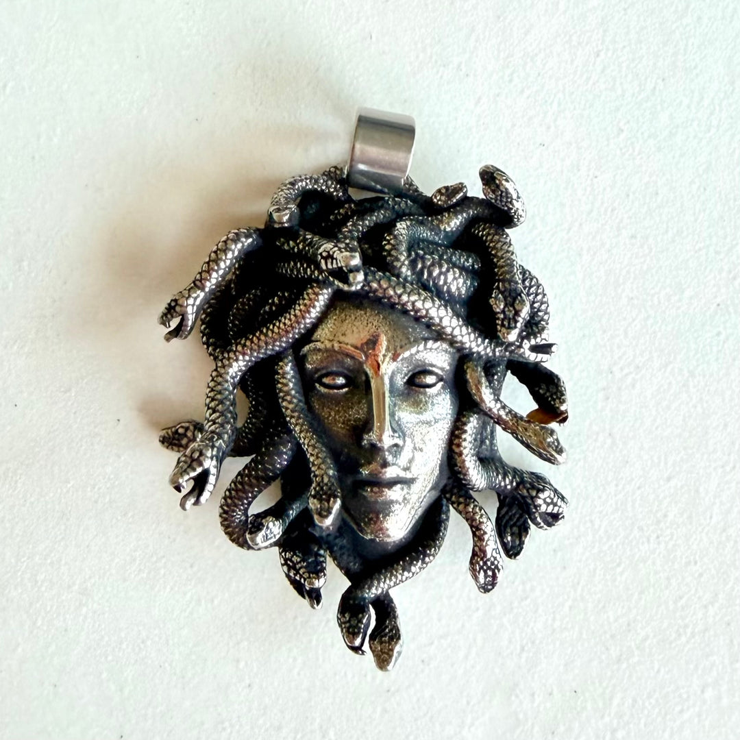 Medusa-riipus vaalealla taustalla edestä kuvattuna, titaaniteräksinen amuletti mustauskäsittelyllä ja korkeakiiltoisella pinnalla.