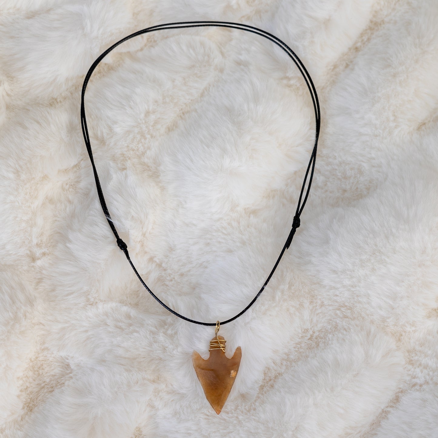 Koko piikivikärkinen kaulakoru, jossa musta tekonahkanyöri, piikivinen nuolenkärki ja kullanvärinen ripustuslenkki. - Full flintstone arrowhead necklace with a black vegan leather cord, flint arrowhead, and gold-colored wire pendant loop.