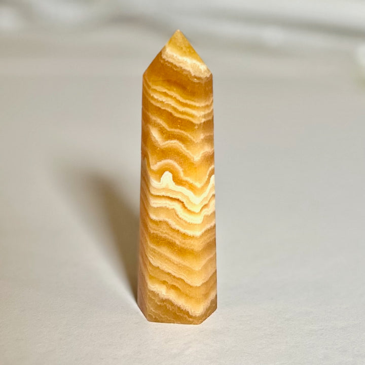 Oranssi kalsiittitorni, sileäksi hiottu ja läpikuultava, jossa lämmin oranssi väri korostaa kiven luonnollista kauneutta. - Orange calcite tower, smoothly polished and translucent, with a warm orange hue highlighting the stone’s natural beauty.