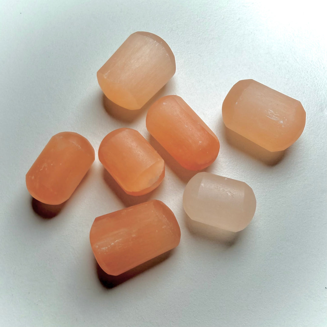 Oransseja seleniitti-kiviä hiottuna lieriön muotoon valkoisella taustalla.