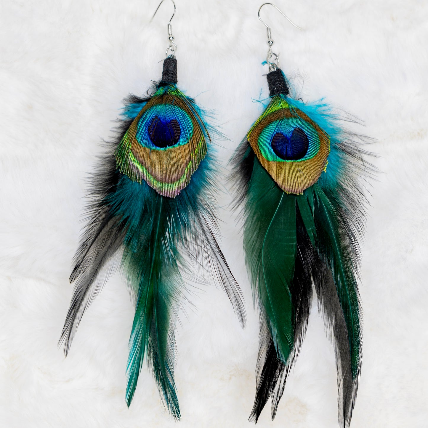 Riikinkukonsulkaiset korvakorut, joissa sulka ja metalliset yksityiskohdat. Symboloi kauneutta, ylpeyttä ja uudistumista. - Peacock feather earrings with a feather and metallic details. Symbolizes beauty, pride, and renewal.