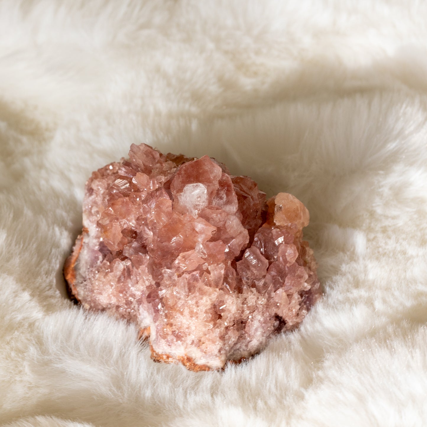 Vaaleanpunaisen ametistin druse lähikuvassa. Kivessä näkyvät kiteet hehkuvat hennon vaaleanpunaisen ja purppuran eri sävyissä, korostaen sen luonnollista kauneutta. - Close-up of a pink amethyst druse. The visible crystals glow in delicate shades of pink and purple, highlighting its natural beauty.