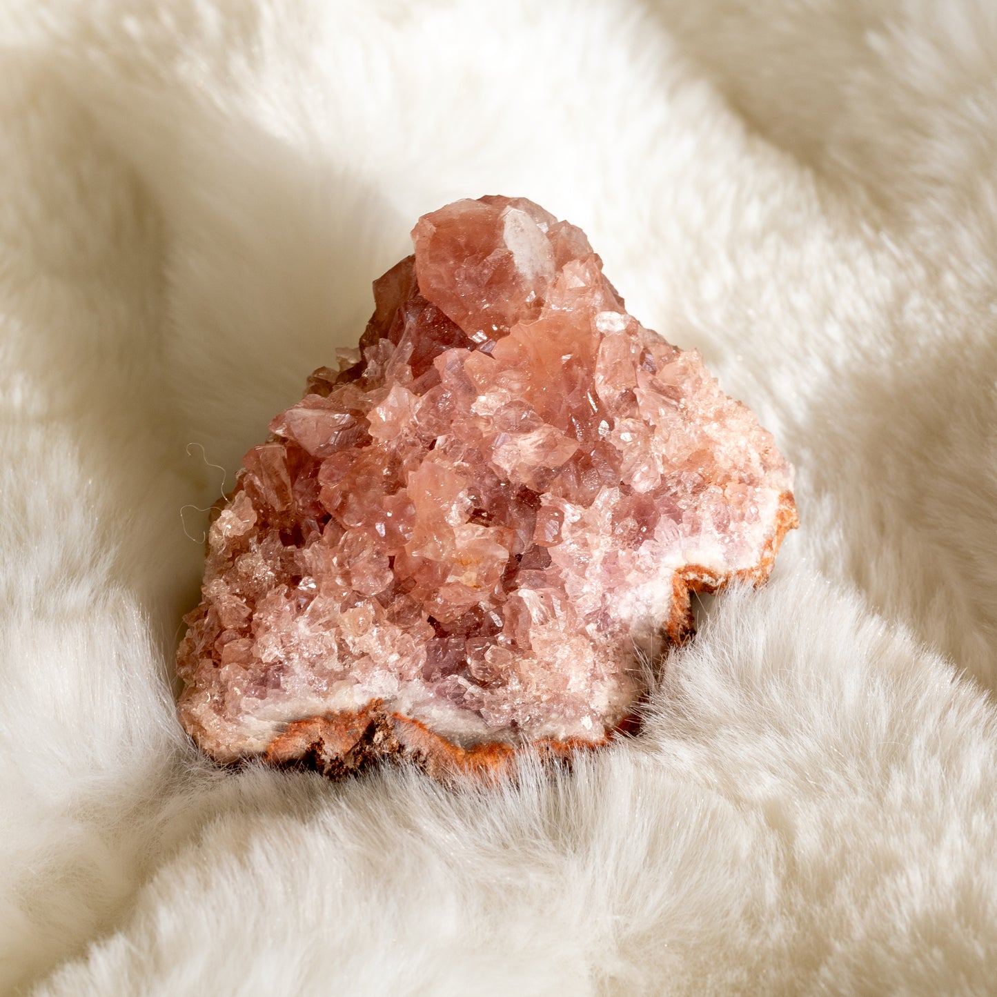 Vaaleanpunaisen ametistin druse lähikuvassa. Kivessä näkyvät kiteet hehkuvat hennon vaaleanpunaisen ja purppuran eri sävyissä, korostaen sen luonnollista kauneutta. - Close-up of a pink amethyst druse. The visible crystals glow in delicate shades of pink and purple, highlighting its natural beauty.