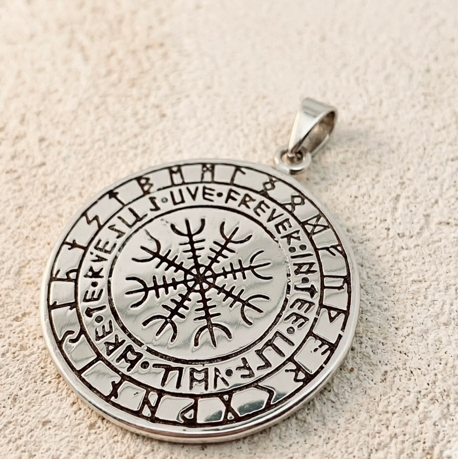 Titaaniteräksisen viikinkiamuletin hopeanhohtoinen kääntöpuoli asetettuna vaalealle, eläväpintaiselle alustalle. Kuva esittää tarkasti koruun kaiverretun maagisen Vegvísir-viikinkikompassin ja sitä ympäröivän riimukehän.