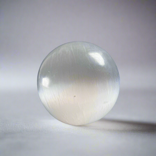 Kirkas ja läpikuultava seleniittipallo, jonka pinta heijastaa valoa silkkimäisesti. - Clear and translucent selenite sphere with a light-reflecting, silky surface.