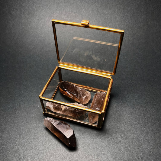 Savukvartsikärkiä raakakristalleina neljä kappaletta lasirasiassa pöydällä - Smoky quartz crstal points, set of four in a glass box on a table.