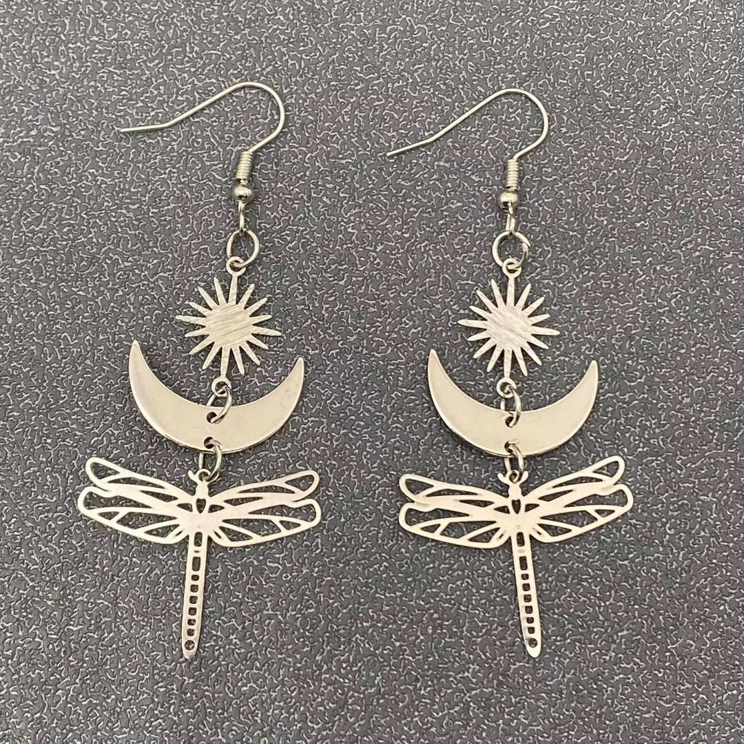 Hopeansävyiset kuparikorvakorut, joissa Aurinko, Kuu ja suuri sudenkorento symboloivat valoa, tunteiden rytmiä ja muodonmuutosta. - Silver-toned copper earrings featuring the Sun, the Moon, and a large dragonfly symbolizing light, the rhythm of emotions, and transformation.