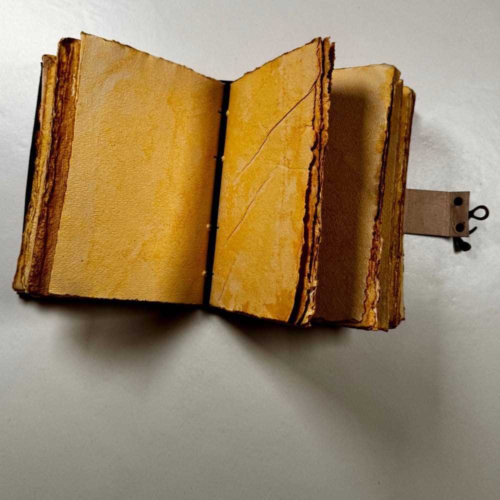 Käsintehty nahkainen muistikirja avattuna – näkyvissä sivuaukeama ja käsintehdyn paperin rustiikkinen tekstuuri. - Handcrafted leather notebook opened – showing a double page spread with the rustic texture of handmade paper.