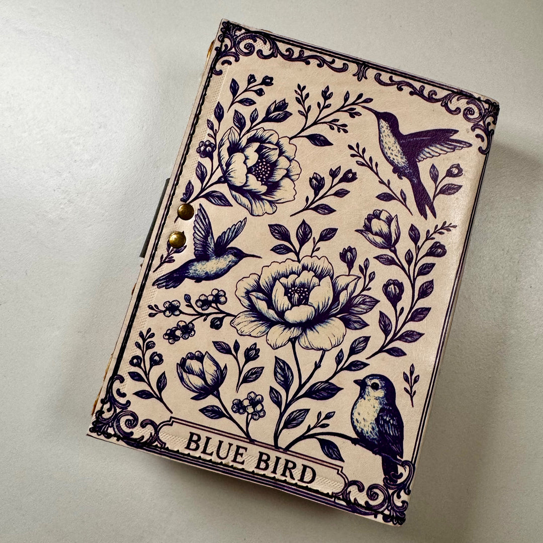 Sinilintuaiheinen nahkakantinen muistikirja takaa kuvattuna, esillä kirjan takakansi. - Blue Bird-themed leather-bound notebook photographed from the back, showing the book’s back cover.