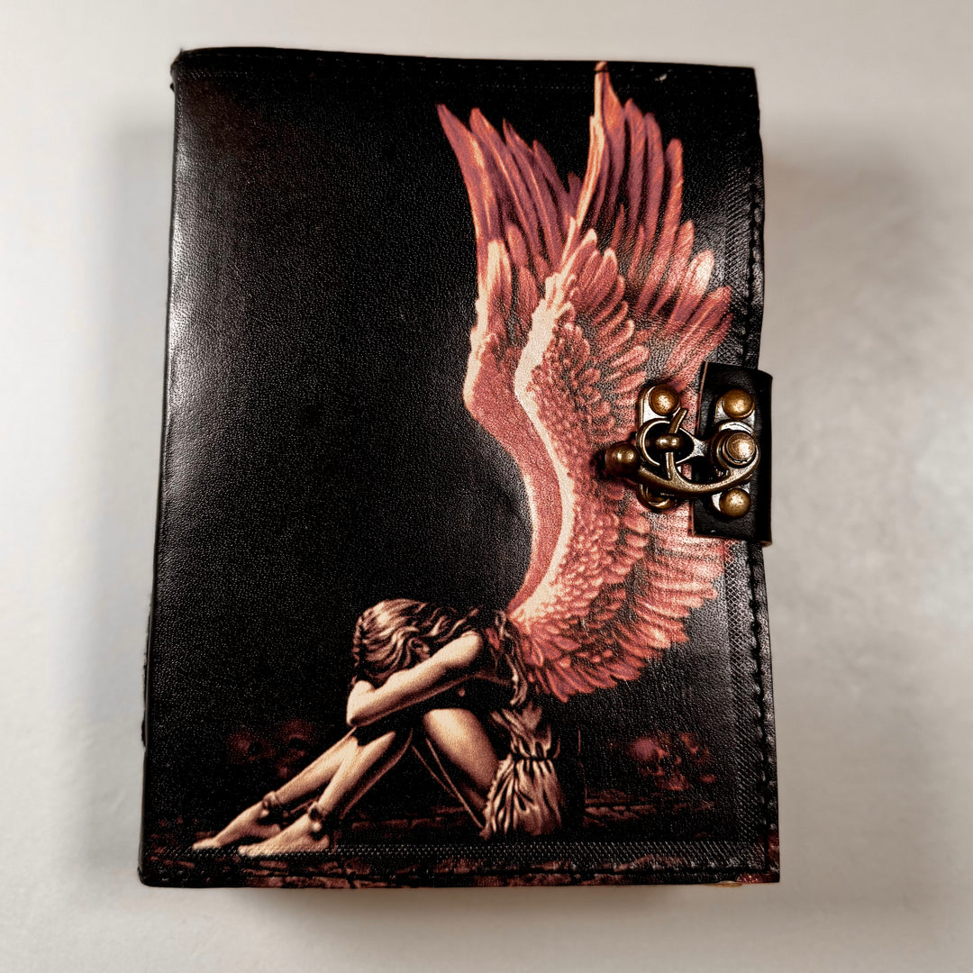 The Broken Angel -muistikirjan etukansi, jossa enkelisymboli ja koristeellinen kohokuviointi. - Front cover of The Broken Angel notebook featuring an angle symbol and embossed decorative details.