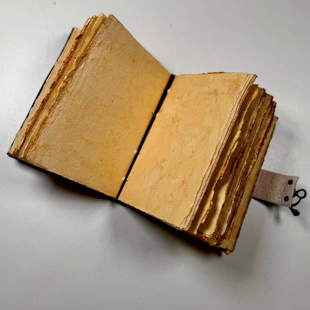 Käsintehty nahkainen muistikirja avattuna – näkyvissä sivuaukeama ja käsintehdyn paperin rustiikkinen tekstuuri. - Handcrafted leather notebook opened – showing a double page spread with the rustic texture of handmade paper.