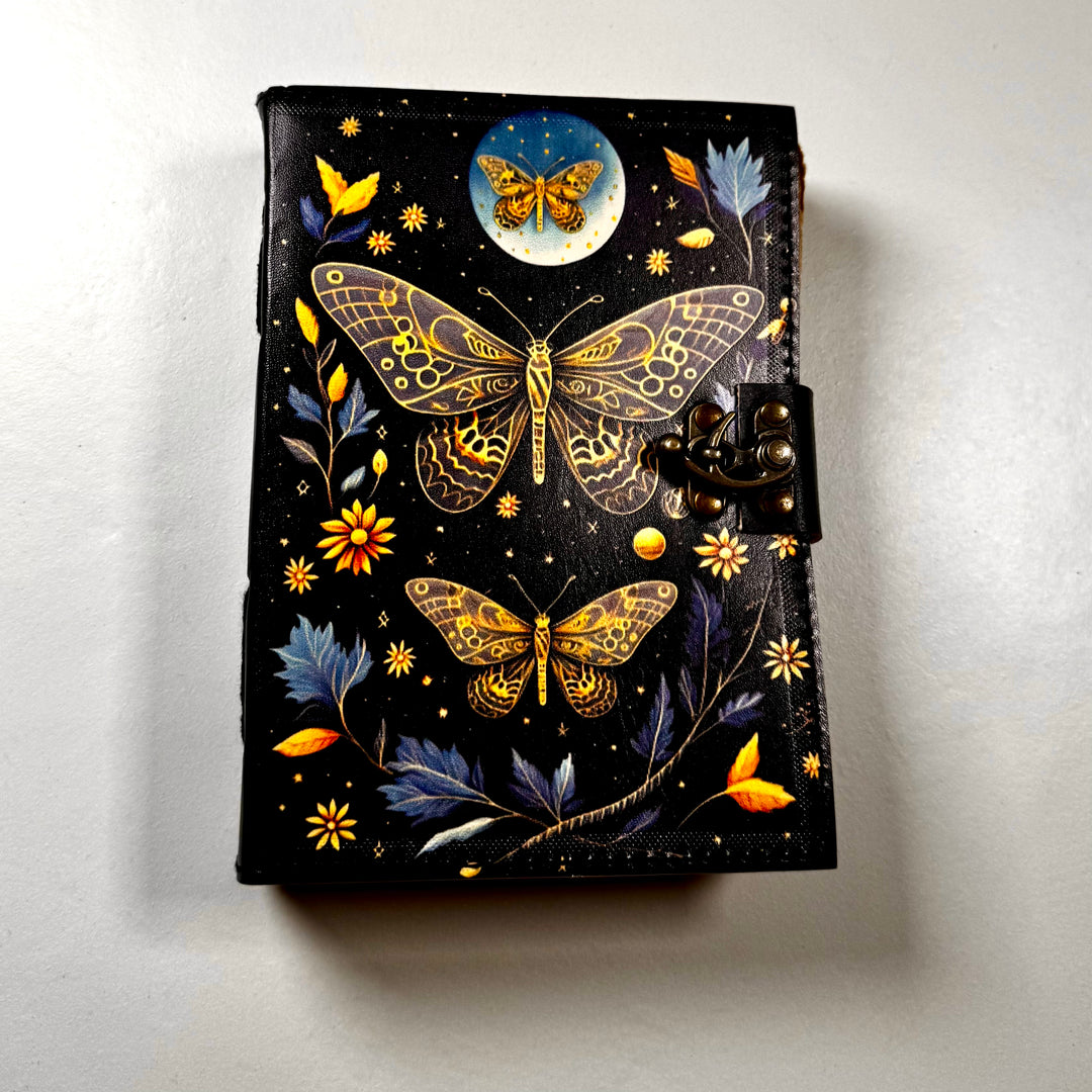 The Goleden Butterfly -muistikirjan etukansi, jossa perhossymboli ja koristeellinen kuviointi. - Front cover of The Golden Butterfly -notebook featuring a butterfly symbol and embossed decorative details.